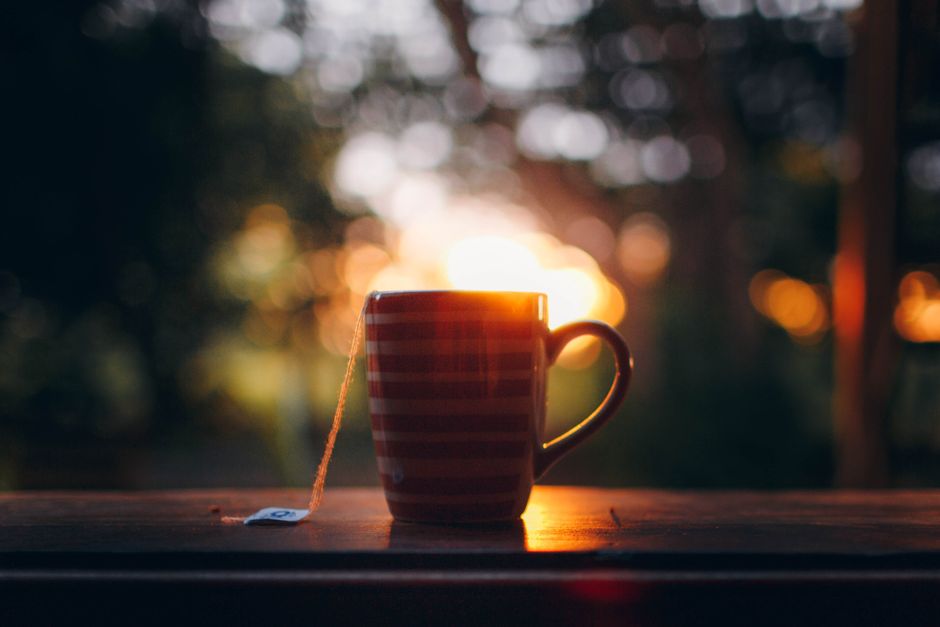 Ceramic mug with teabag placed on wooden table against blurred green park during sunset
