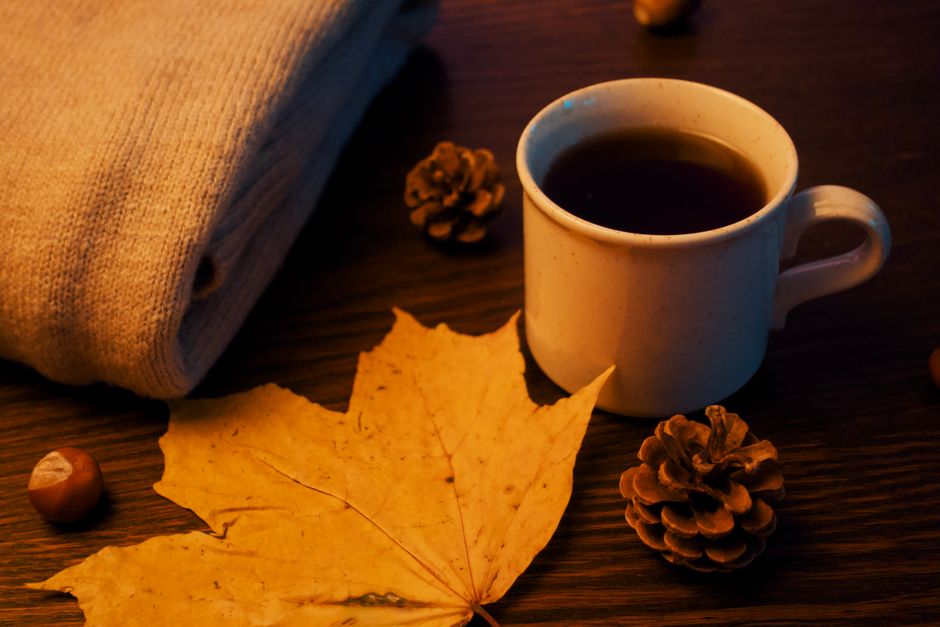 Warm autumn setup with tea, pinecones, and a fall leaf on a wooden table.
