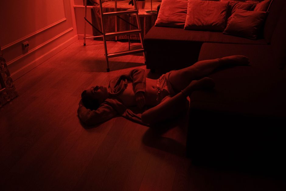 A person is lying on the floor in a dimly lit room with red lighting, capturing a serene yet dramatic mood.