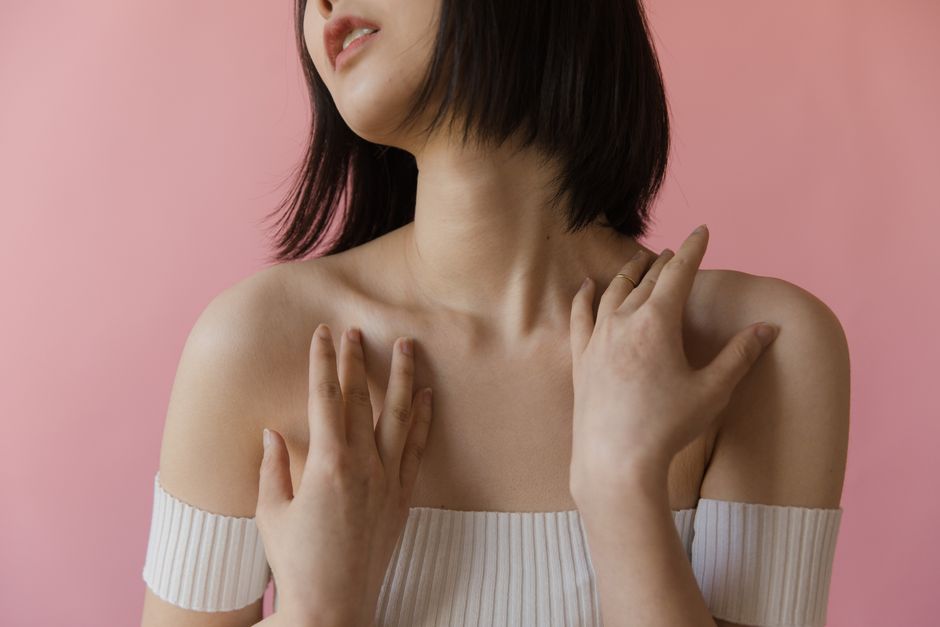 Elegant portrait of a woman touching her shoulders against a soft pink background.